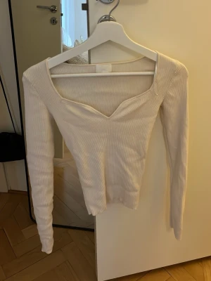 Ribbad ljusrosa topp från H&M - Säljer en ribbad ljusrosa långärmad topp från H&M med snygg v-ringning och figurnära passform. Perfekt att styla med jeans eller kjol för en trendig look. Materialet är mjukt och stretchigt för extra komfort.