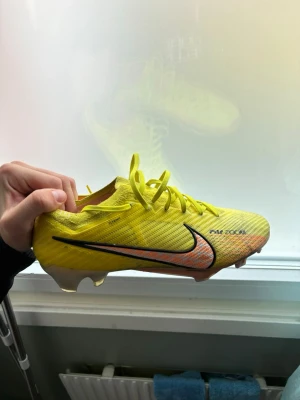 Nike Mercurial gul fotbollssko - Säljer ett par Nike Mercurial fotbollsskor i en skarp gul färg med svart och orange swoosh på sidan. Skorna har snörning och är tillverkade i ett lätt syntetmaterial för bästa bollkontroll och grepp på planen. Perfekta för dig som vill sticka ut på fotbollsplanen.