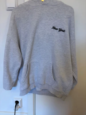 Grå hoodie med New York-tryck - Snygg oversize hoodie från pull and bear, den har tyvärr en liten fläck men den syns inte så mkt. 