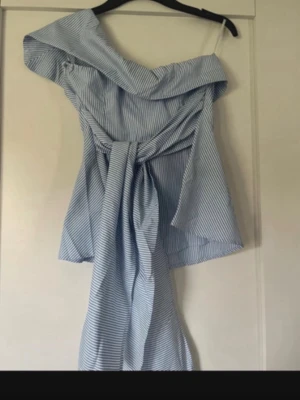 Blåvit offshoulder omlottklänning - Snygg blåvit kortklänning med smala ränder och offshoulder-design. Klänningen har omlottknytning i midjan och en luftig passform. Perfekt för varma dagar och ger en fräsch sommarkänsla. Ifrån SHEIN