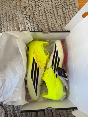 ADIDAS F50 ELITE FG - GUL/SVART - Säljer ett par Adidas F50 Elite FG fotbollsskor i neon-gult och vitt med svarta och röda detaljer. Storlek 42. Skorna är helt oanvända. Kartong, påse och extra sulor följer med. Nypris 3099kr!