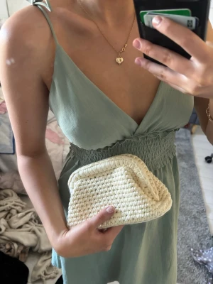 Beige virkad kuvertväska - Säljer en beige kuvertväska i virkat material. Väskan har en mjuk, rektangulär form med stadig ram upptill och stängs med ett klassiskt metallspänne. Perfekt för dig som gillar en stilren och trendig accessoar.