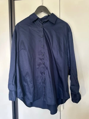 Mörkblå oversized skjorta i storlek S - Snygg mörkblå skjorta i oversized modell med klassisk krage och knappar framtill. Skjortan har långa ärmar och är tillverkad i ett mjukt bomullstyg som känns skönt mot huden. Perfekt att styla lager på lager eller bära som den är.