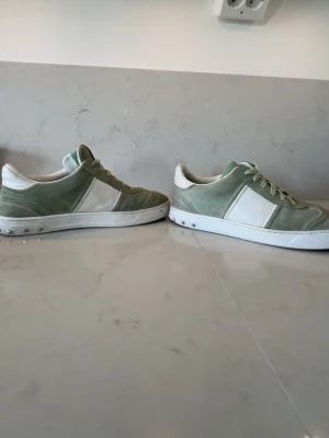 Grönvita sneakers i mocka - Snygga sneakers i ljusgrön mocka med vita detaljer och vit sula. Klassisk låg modell med snörning och stilren design. Perfekta för dig som gillar en clean och avslappnad look.