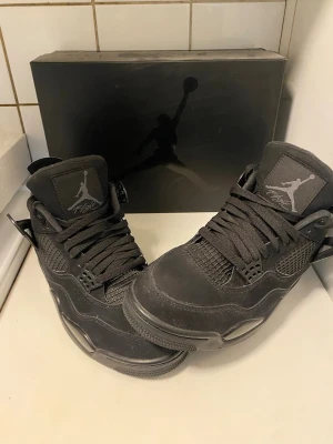 Black Cats Jordan 4 Retro  - Snygga helsvarta Black Cats Jordan 4 Retro sneakers som är super eftertrakade med ikonisk Jumpman-logga på plösen. Skorna har en robust sula, meshdetaljer på sidorna och ovandel i mocka. Klassisk snörning och plastdetaljer vid snörhålen ger en sportig vibe. Låda och tillbehör ingår såklart. För mer frågor är det bara att höra av sig i dm! 