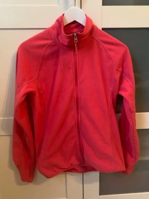 Rosa fleecejacka med dragkedja - Snygg rosa fleecejacka med hel dragkedja och hög krage. Perfekt för lager-på-lager och håller dig varm under kyliga dagar. I jättefint skick. Storlek 36