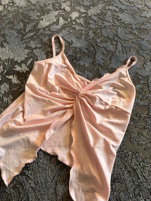 Ljusrosa satin - Säljer en ljusrosa i satin med tunna axelband och twistad detalj framtill. Toppen har en glansig finish och asymmetrisk nederkant som ger en extra touch. Perfekt för mysiga kvällar hemma.