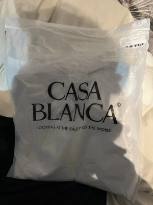 Svart t-shirt från Casablanca - Snygg svart t-shirt från Casablanca med stort grafiskt tryck i blå toner och texten 'CASA BLANCA' på framsidan. Klassisk passform och rund hals. Perfekt för dig som gillar stilrena och moderna plagg. Kom privat för kvitto