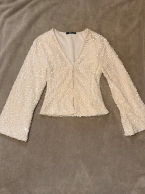 Paljettprydd vit topp från Gina Tricot - . Säljer en superfin vit topp från Gina Tricot med paljetter över hela plagget. Toppen har v-ringning och långa ärmar, perfekt för dig som vill sticka ut. Den har en lätt figurnära passform och känns riktigt lyxig.