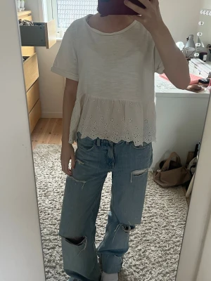 Vit blus med volang  - Söt vit blus med korta ärmar och volang nedtill. Nederdelen har jättefina broderade blommönster. Tröjan har också en superliten fläck som man knappt ser (ser på sist bilden, går förmodligen bort i tvätten). Skriv ifall fler frågor!🩷🩷🩷