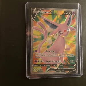Pokémonkort Espeon V Full Art - Säljer ett Pokémonkort Espeon V Full Art med 200 HP. Kortet har färgstark design med Espeon i lila och gult, och är inplastat i ett skyddsfodral. Kortet har attackerna Zen Shot och Super Psy Bolt. Perfekt för samlare eller Pokémonfans!