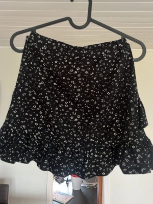 Svart blommig volangkjol från Kappahl  - Storlek 146/152 men passar också XS/S då den är väldigt stretchig. Supersöt svart kortkjol med små vita blommor och volangkant nedertill. Kjolen har en luftig och lätt känsla, perfekt för varma dagar. Pris kan självklart diskuteras!