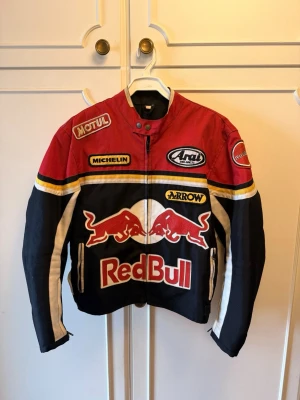 Nostalgisk Red Bull racing jacka :) - Snygg racinginspirerad jacka från Red Bull med broderade loggor och patchar från bland annat Motul, Michelin och Arrow. Jackan har dragkedja framtill, långärmad design och färger i rött, svart, vitt och gult. Perfekt för dig som gillar motorsport och streetwear.
