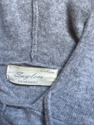 Grå cashmere hoodie från Styles - Mjuk och stilren hoodie i grått från Styles, tillverkad i lyxig cashmere. Klassisk modell med huva och dragsko, samt ribbade muddar vid ärmslut och nederkant. Perfekt för dig som gillar en enkel men exklusiv look. Passar dig som är runt 160-165. Vid frågor så är de bara att ställa! 