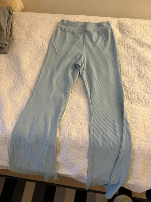Två par loungebyxor i blått och grått - Säljer två par mjuka loungebyxor, ett par ljusblå ribbade och ett par ljusgrå släta. Båda har bred resår i midjan och raka ben, perfekta för chill hemma. Materialet känns stretchigt och bekvämt, passar dig som gillar avslappnad stil.