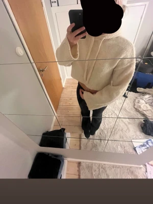 stickad hoodie - Mysig krämvit stickad hoodie med luva och dragsko. Tröjan har en croppad passform, vida ärmar och ribbade muddar vid ärmslut och nederkant. Perfekt för dig som gillar en avslappnad och trendig stil.