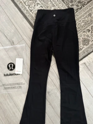 Svarta flare leggings  - Snygga svarta leggings med hög midja och utsvängda ben. Tillverkade i ett stretchigt och mjukt material som sitter skönt på kroppen. Perfekta för både träning och chill. Diskret logga framtill i midjan. Kommer med originalpåse och tag kvar.