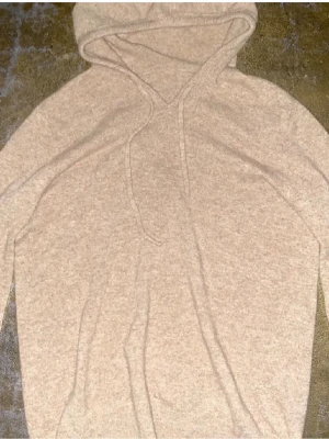 Beige hoodie i mjukt material - Säljer en beige hoodie med huva och dragsko. Hoodien är tillverkad i ett mjukt, stickat material som känns riktigt skönt mot huden. Perfekt för dig som gillar en enkel och clean stil. Inga synliga loggor eller tryck.