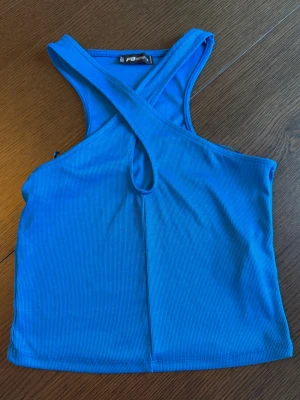 Blå ribbad linnetopp  - Snygg blå ribbad linnetopp med korsad design framtill. Toppen är ärmlös och croppad, perfekt för varma dagar eller lager på lager. Materialet är mjukt och stretchigt för en bekväm passform.