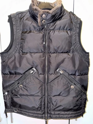 Svart dunväst från Parajumpers - Snygg svart dunväst från Parajumpers med hög krage och mjukt foder. Västen har två stora fickor med dragkedja och knapp, samt detaljer i metall. Perfekt för lager-på-lager och har en sportig, modern look. Autentisk.