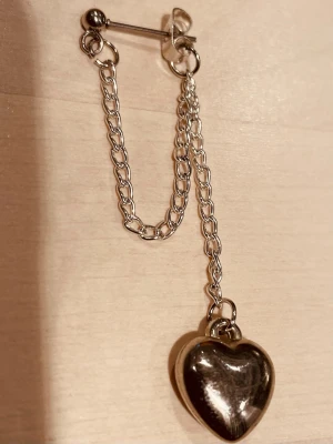 By prisförslag- 1 st Silverfärgat örhänge med hjärthänge - Säljer ett snyggt silverfärgat örhänge med kedjedetalj och ett blankt hjärthänge. Örhänget har en cool design med dubbla kedjor och passar perfekt för dig som gillar statement-smycken. Materialet är metall i silverton.