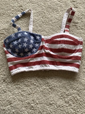 Randig korsettopp med stjärnor - Snygg korsettopp med breda axelband och dragkedja bak. Toppen har amerikanskt flaggmönster med röda och vita ränder samt blått parti med vita stjärnor. Perfekt för dig som vill sticka ut!