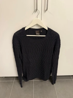 Mörkblå stickad tröja från Oscar Jacobsson, stl L - Snygg mörkblå stickad tröja från Oscar Jacobsson med ett diskret diamantmönster över hela tröjan. Rund halsringning och ribbade muddar vid ärmslut och nederkant. Perfekt för lager på lager och enkel att matcha med jeans eller kjol.