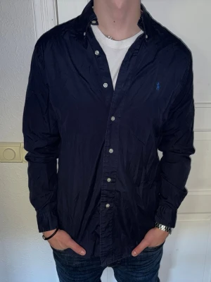 Mörkblå skjorta från Ralph Lauren - Mörkblå skjorta från Ralph Lauren i storlek M.  Fint skick till ett bra pris. Nypris: 1995kr. Mitt pris: 349kr. Vid frågor eller funderingar, tveka inte att höra av dig.