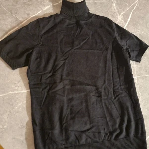 Svart polotopp från bpc selection - Klassisk svart polotopp från bpc selection med korta ärmar och ribbad polokrage. Toppen har en enkel och stilren design som passar till många olika looks. Tillverkad i mjukt material för en bekväm känsla.