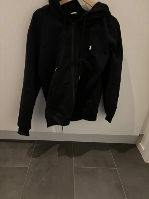 Svart hoodie från Polo Ralph Lauren - Snygg svart hoodie från Polo Ralph Lauren med dragkedja framtill och klassisk logga på bröstet. Hoodien har huva med dragsko och praktiska fickor på magen. Perfekt för en avslappnad och stilren look.