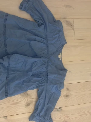 Blå blus från Gina Tricot - Söt blå blus från Gina Tricot med trekvartsärm och dekorativa spetsdetaljer. Blusen har en avslappnad passform och rund halsringning. Perfekt att styla med jeans eller kjol för en trendig look.