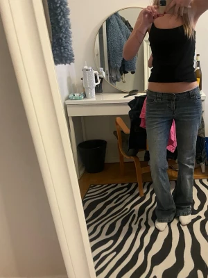 Blå bootcut jeans  - Säljer ett par blå bootcut jeans med klassisk kontrastsöm och broderad ficka bak. Jeansen har låg midja och slitna detaljer för en cool vintagekänsla. Perfekta till sneakers eller boots för en avslappnad look.