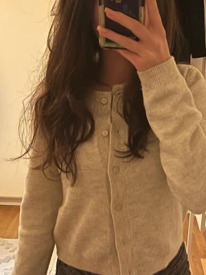 Beige kofta med knappar - Mysig beige kofta med rund hals och knäppning framtill. Tröjan har långa ärmar och ribbade muddar vid ärmslut och nederkant. Perfekt att slänga på sig över en topp eller t-shirt.