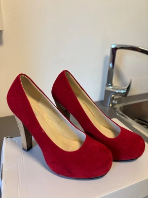 Röda pumps med träklack - Snygga röda pumps i mockaimitation med rund tå och träfärgad klack. Klackarna är i bra skick och ungefär 6-10 cm lång klack.  