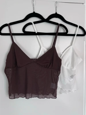 2 linnetoppar i mesh brun & vit, storlek M & S - Säljer två linnetoppar i mesh, en chokladbrun och en vit. Båda har tunna axelband, v-ringad front och vågig kant nedtill. Den vita är omlott.