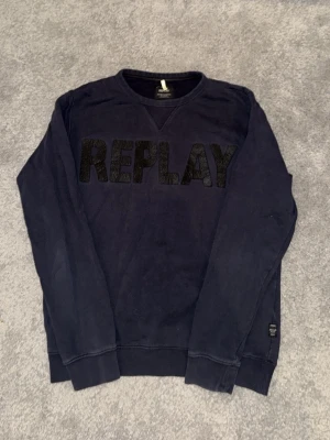  Replay sweatshirt  - Mörkblå sweatshirt från Replay med stor svart REPLAY-logga framtill. Tröjan har rund halsringning, långa ärmar och ribbade muddar vid ärmslut och nederkant. Perfekt för en avslappnad och trendig look.