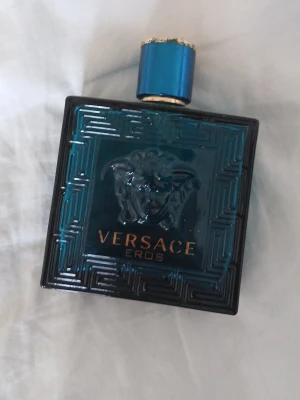 Versace Eros parfym blå glasflaska inget i du kan fylla på saker i den - Versace Eros parfym i en snygg, fyrkantig blå glasflaska med gulddetaljer och Medusa-huvud på framsidan. Flaskan har ett coolt mönster och ett matchande blått lock med guldkant. Perfekt för dig som gillar exklusiva dofter och stilren design.