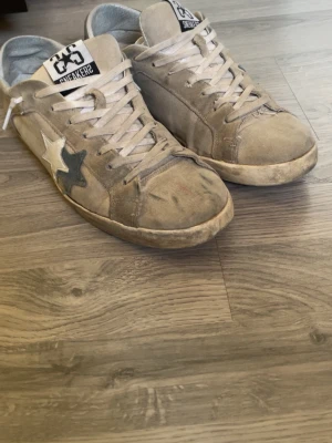 Beige sneakers från 2star med stjärna - Säljer ett par beige sneakers från 2 star med vit och grå stjärndetalj på sidan. Skorna har vita snören, låg profil och är tillverkade i mocka. Klassisk streetstil med tydlig logga på plösen och en slitstark gummisula. Släppt lite på sidorna och är inte i jätte bra skicka men hör av dig vid frågor. Mvh