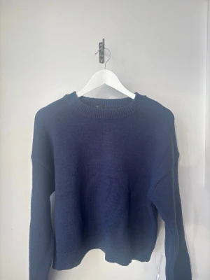 Mörkblå stickad tröja ASOS desgin - Mysig mörkblå stickad tröja från asos design  med rund halsringning och ribbade muddar. Tröjan har en avslappnad passform och är perfekt för lager på lager. Materialet ser ut att vara mjukt och skönt, troligen en ull- eller akrylblandning.