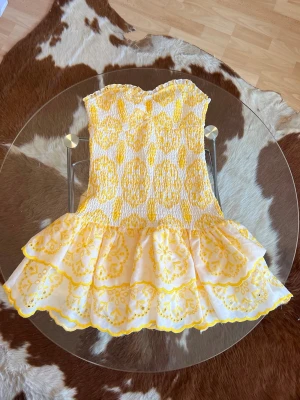 Gul och vit volangklänning - Supersöt kort klänning i vitt och gult med broderade blommönster och volangkjol.             Köpte av en tjej på Vinted som ska ha köpt den i Spanien. Men tyvärr passar den inte mig, därav säljer jag💛(enbart tests av mig, använd 1 gång av förra ägaren)