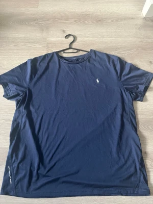 Mörkblå t-shirt från Polo Ralph Lauren - Snygg mörkblå träningströja Polo Ralph Lauren med klassisk logga broderad på bröstet. T-shirten har rund halsringning och korta ärmar. Tillverkad i mjukt material som känns skön mot huden. Perfekt till när du ska träna