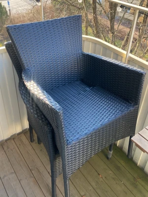 Svarta konstrottingstolar stapelbara - Två svarta stolar i konstrotting med armstöd och hög rygg. Stolarna är stapelbara och passar perfekt till balkong eller uteplats. Modern flätad design och robust metallram ger stabilitet och stil till din utomhusmiljö.