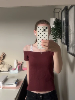 Vinröd offshoulder topp - Trendig vinröd offshoulder topp med korta ärmar och ribbad struktur. Toppen har en smickrande, tight passform och är perfekt för dig som gillar en enkel men snygg stil. Materialet känns mjukt och stretchigt, vilket gör den bekväm att bära hela dagen.