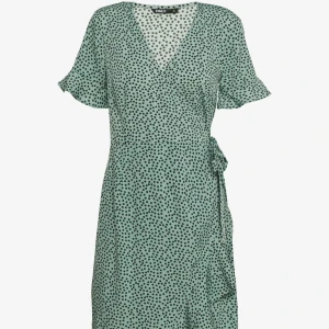 Grön prickig omlottklänning från ONLY - Superfin grön omlottklänning från ONLY med mörk gröna prickar, v-ringning och knyt i midjan. Klänningen har korta ärmar med lätt volang och är i en luftig modell som passar perfekt till varma dagar. Snygg och bekväm att bära hela sommaren!💕💕💕