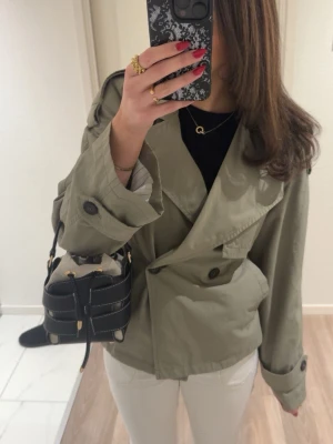 Grön trenchcoat från Bershka - Jättesnygg trenchcoat från bershka med band runt midjan. Perfekt nu till våren. Är i nyskick, endast använd två gånger. I storlek 36/s. Hör av er för bilder med den på!