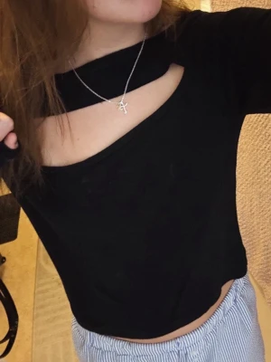 Svart topp med cut out - Trendig svart topp med unik cut out-detalj över bröstet. Toppen har långa ärmar och är perfekt för dig som vill sticka ut med en cool och modern stil.