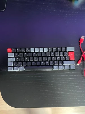 NOS kompakt mekaniskt tangentbord - Säljer ett kompakt mekaniskt tangentbord från NOS med grå, svarta och röda tangenter. Tangentbordet har en minimalistisk design och ansluts via en röd USB-kabel. Perfekt för dig som vill ha ett smidigt och snyggt tangentbord till datorn.