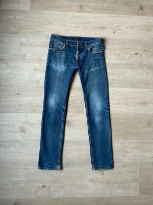 Blåa Dry Denim Nudie Jeans Grim Tim W32 L32 - Fina Nudie Jeans i blå färg. Jeansen är i mycket bra skick och sparsamt använda. |  Äkta som allt annat jag säljer! ✅ |  Storlek: W32 | Skick: Mycket bra skick | Färg: Blå | Märke: Nudie Modell: Jeans |  Hör gärna av dig vid frågor så svarar jag så fort jag kan! 😁|   (Sku - 54)