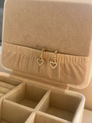 Guldiga örhängen med pärlor och hjärta - Säljer ett par små guldiga hoop-örhängen med pärldetaljer. Guldiga med hängande hjärtan!