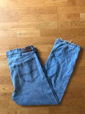 Ljusblå raka jeans med rå kant - Säljer ett par ljusblå jeans med rak passform och rå, fransig kant nedtill. Klassisk femficksmodell i denim med bälteshällor och bakfickor med dekorativ söm. Perfekta för en avslappnad och trendig look.